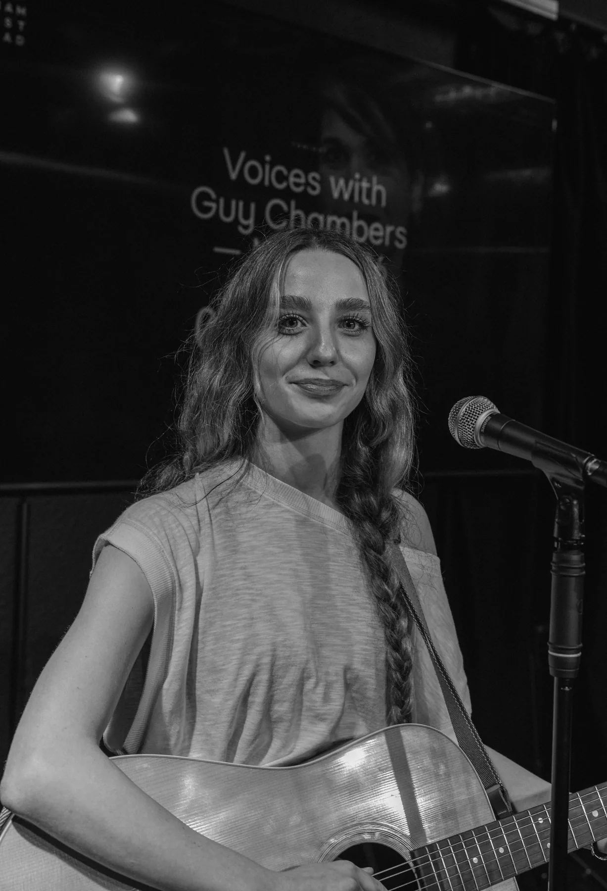 A guitarist on stage beneath the VOICES screen