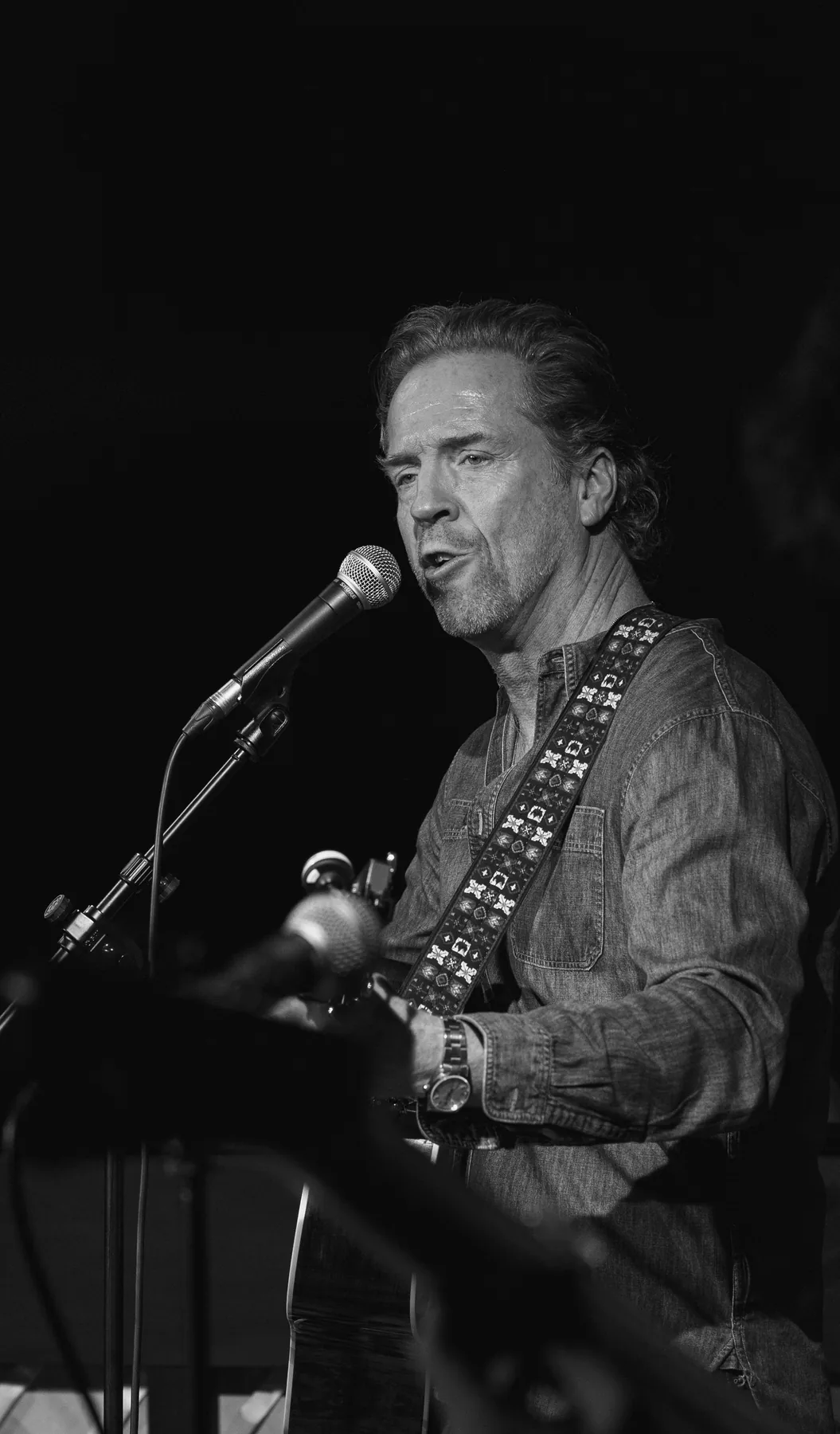 A singer at the microphone, guitar strapped on